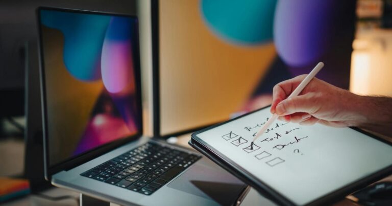 Persona marcando checklist en tableta digital frente a pantallas de trabajo. Imagen conceptual de estrategia de negocios y revisión de procesos.