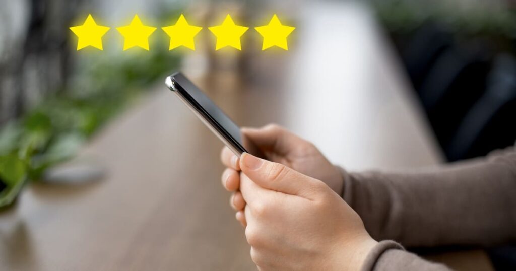 Persona sosteniendo un celular con estrellas de cinco puntos flotando sobre la pantalla, representando una reseña positiva.