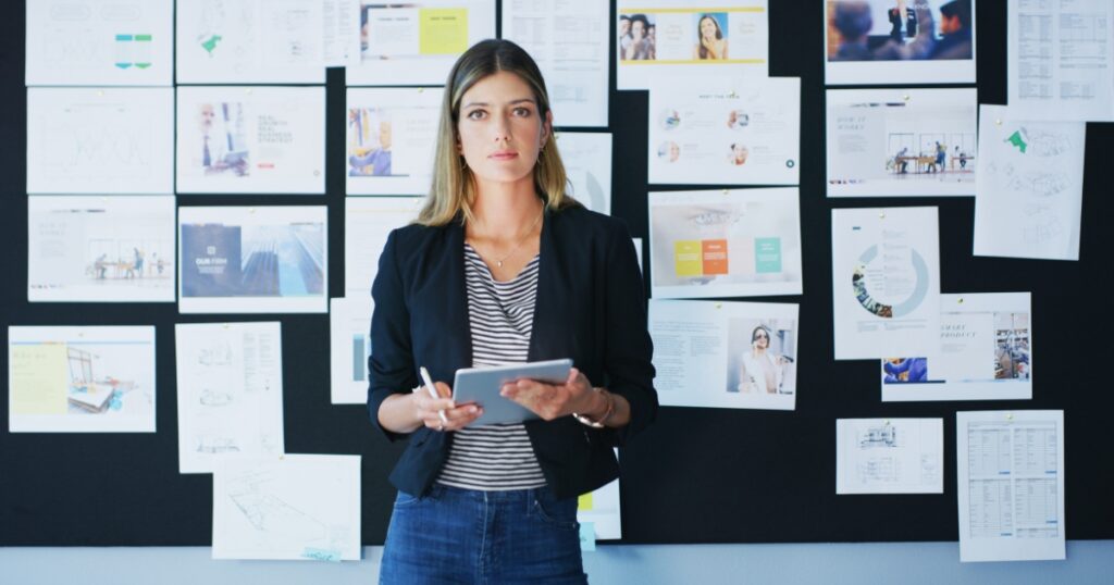 Mujer profesional analizando estrategias de negocio frente a una pared llena de gráficos y documentos.