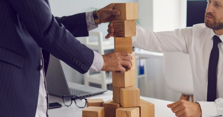 Empresarios construyendo una estructura con bloques de madera, simbolizando planificación y estrategia de negocio.