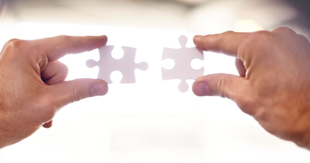 Dos manos sosteniendo piezas de rompecabezas blancas a punto de unirse, simbolizando la coherencia e integración en el branding.